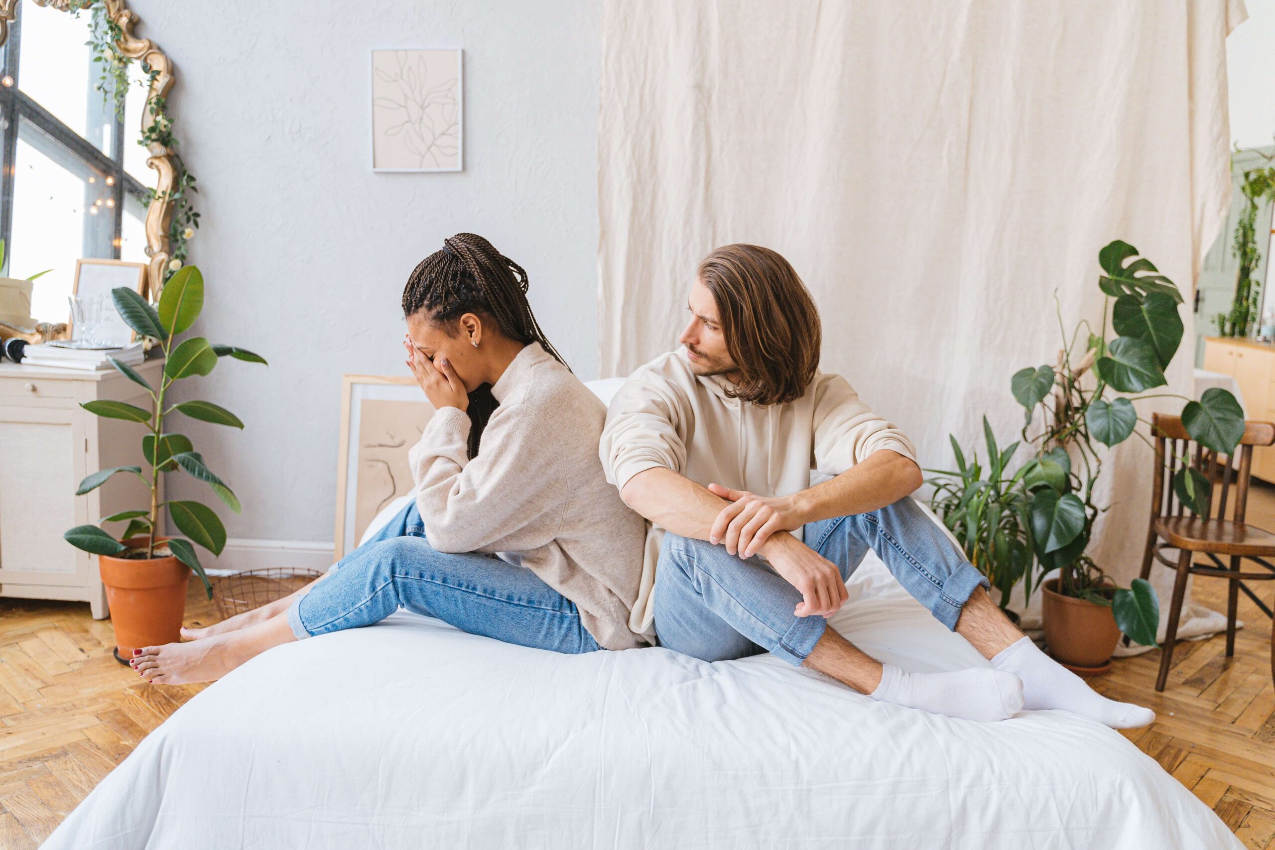 Emotional Invalidation - validation in relationships denver co - individual relationship counseling denver co - therapy for validation in relationships denver co - colorado Couple sitting on a bed, with the woman holding her face in her hands while the man looks at her, representing relationship anxiety and emotional disconnection addressed through validation in relationships in Denver, CO.