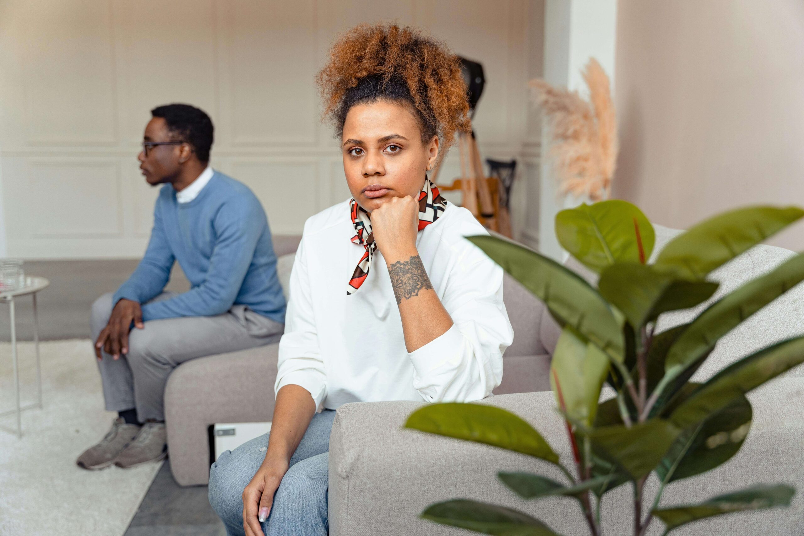 Couple sitting in a counseling session, with the woman looking uncertainly toward the camera while the man sits in the background, representing challenges explored in individual relationship therapy for self-confidence in Denver, CO.