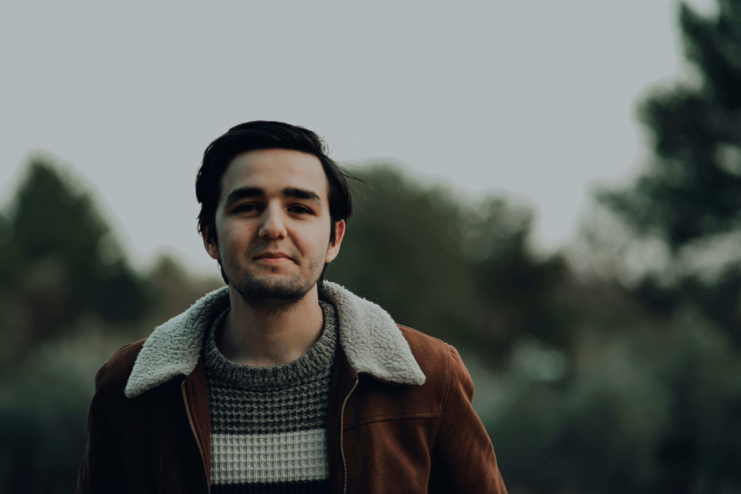 Man standing outdoors in a brown jacket smiling warmly, symbolizing progress and connection through men’s individual relationship counseling in Denver, CO.
