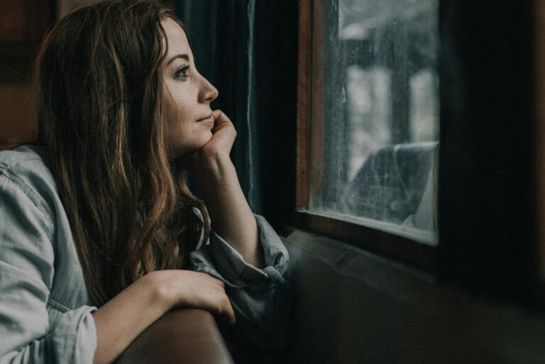 Woman looking out a window on a cloudy day, reflecting on personal growth supported by individual relationship counseling in Denver, CO.