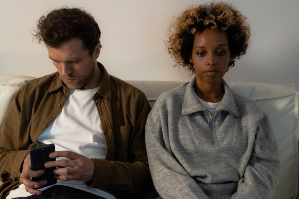 Woman sitting beside her boyfriend while he looks at his phone, illustrating emotional disconnection explored with an individual relationship counselor in Denver, CO.