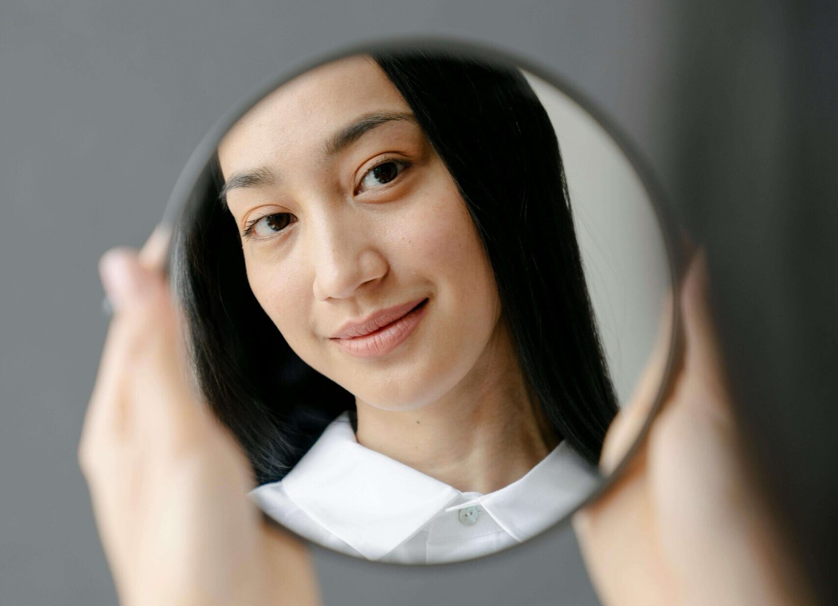 Woman smiling at herself in a mirror, symbolizing self-worth and healing through individual relationship therapy for self-confidence in Denver, CO.