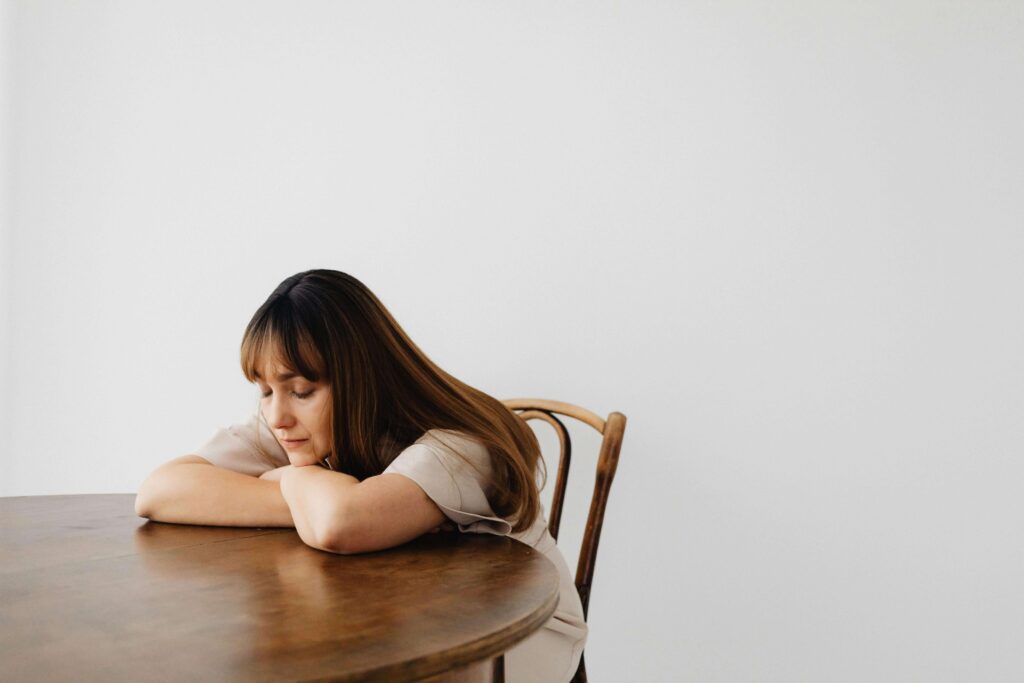 Woman sitting at kitchen table looking sad, representing someone who may benefit from counseling for autistic adults in Denver, CO.