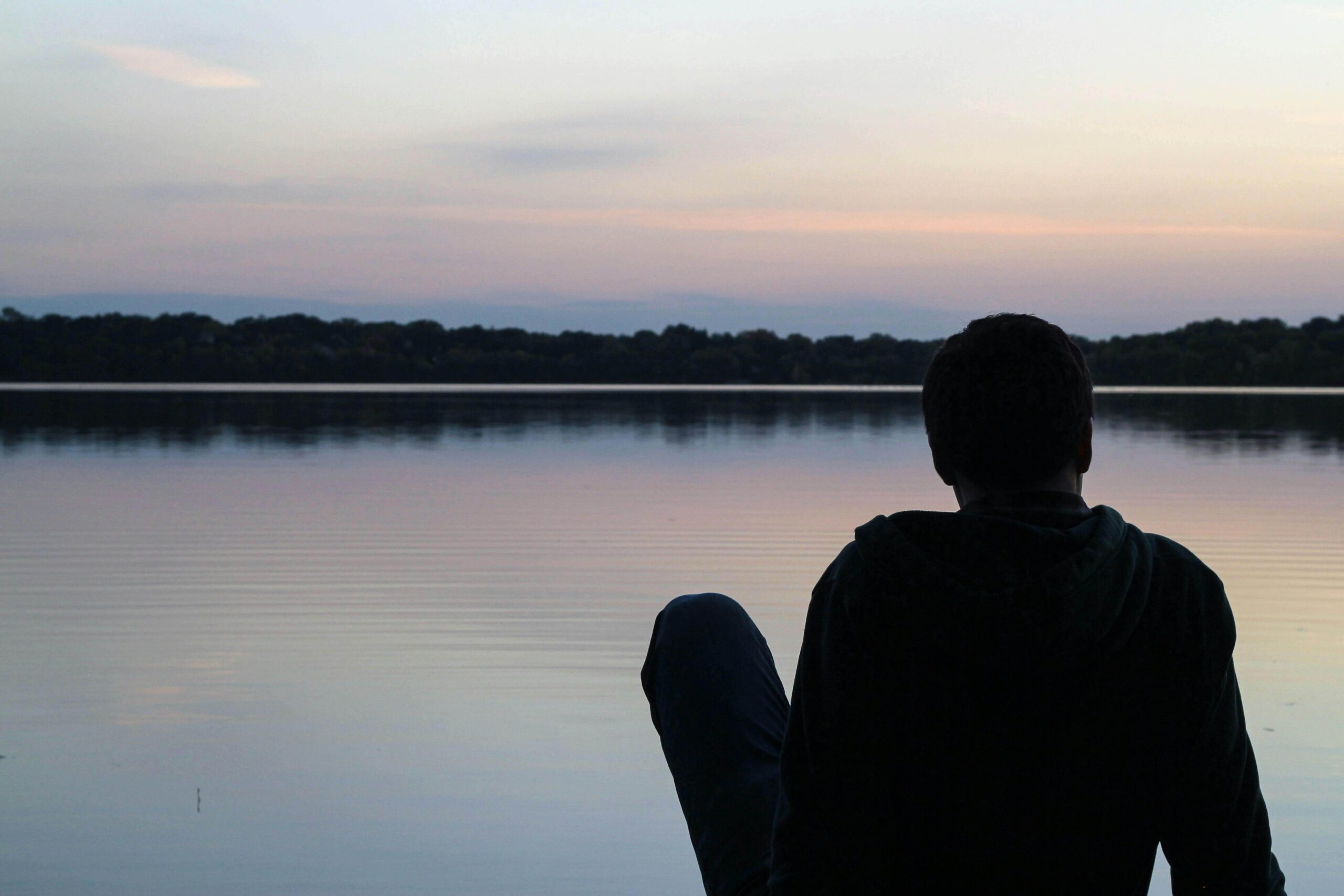Silhouette of a man sitting in front of a lake, illustrating introspection and emotional distance addressed in individual relationship therapy for men with autism in Denver, CO.