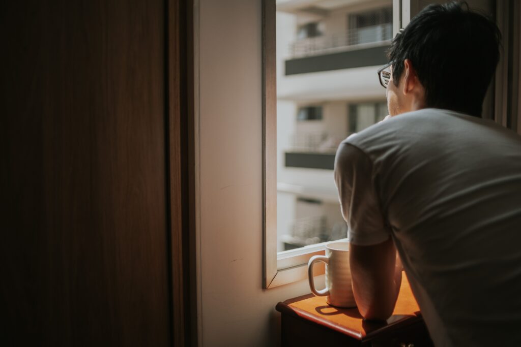 Man gazing out a window in reflection, illustrating relationship patterns and self-worth concerns explored in individual relationship therapy for validation in relationships in Denver, CO.