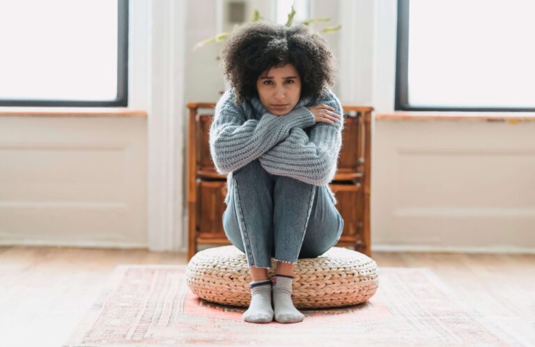 Woman sitting alone on a floor cushion with an insecure expression, representing emotional vulnerability addressed in individual relationship counseling for emotional security in Denver, CO.
