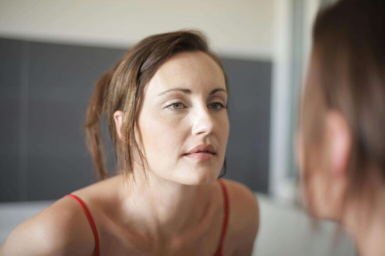 Woman looking at herself thoughtfully in a mirror, representing self-awareness developed in individual relationship therapy for self-confidence in Denver, CO.
