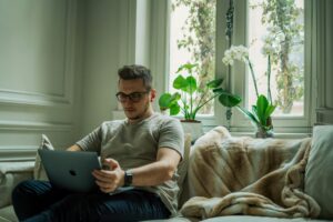 Person sitting on a couch with a laptop, appearing thoughtful in a calm home setting, representing individual relationship counseling in Denver, CO.