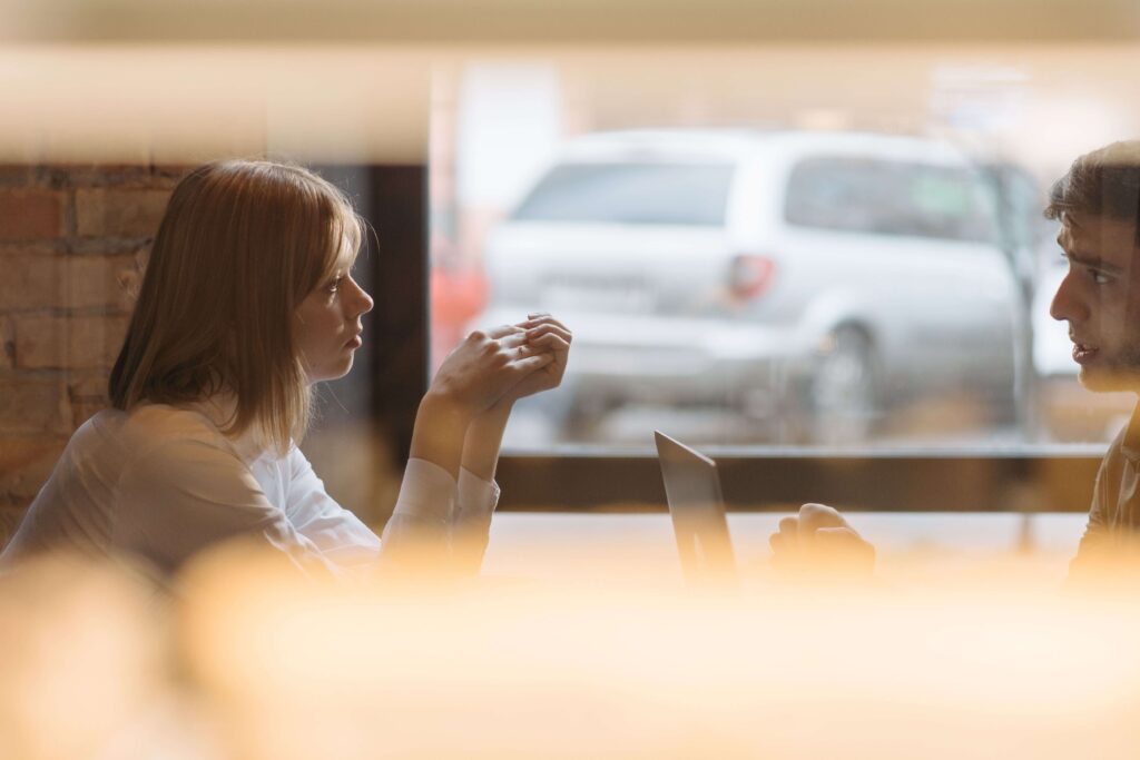 Man and woman sitting at a table, with the woman appearing withdrawn and disconnected, illustrating relationship patterns addressed through individual relationship counseling in Denver, CO.