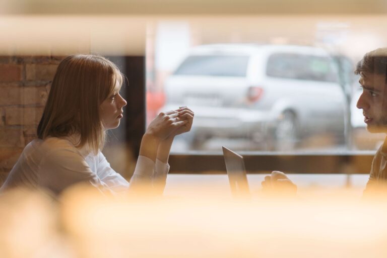 Man and woman sitting at a table, with the woman appearing withdrawn and disconnected, illustrating relationship patterns addressed through individual relationship counseling in Denver, CO.
