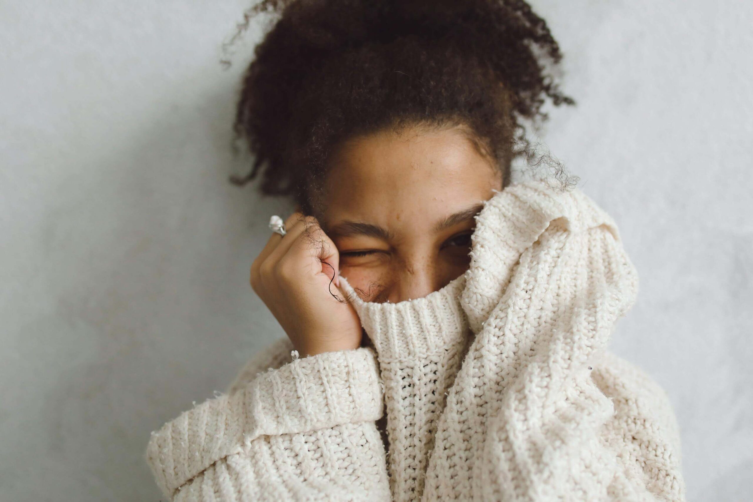 Woman covering part of her face with a sweater while smiling with her eyes, symbolizing growing confidence through self-esteem counseling in Denver, CO.