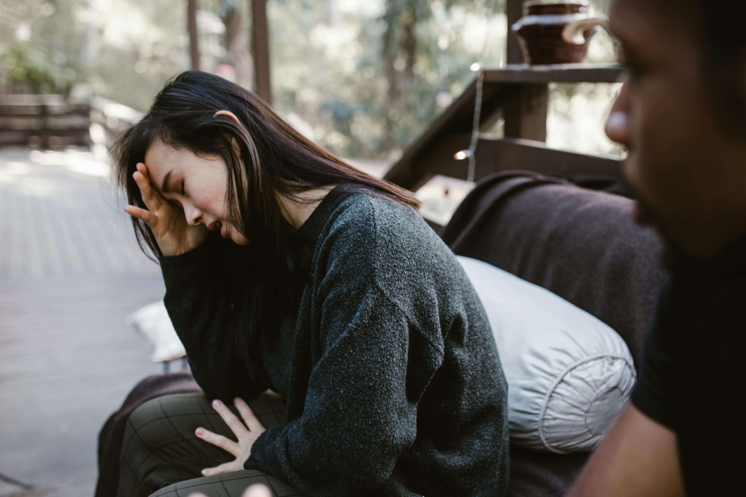 Woman with her hand on her forehead and eyes shut looking distressed while a man sits nearby out of view, representing challenges explored in individual relationship therapy for women seeking long-term relational healing in Denver, CO.