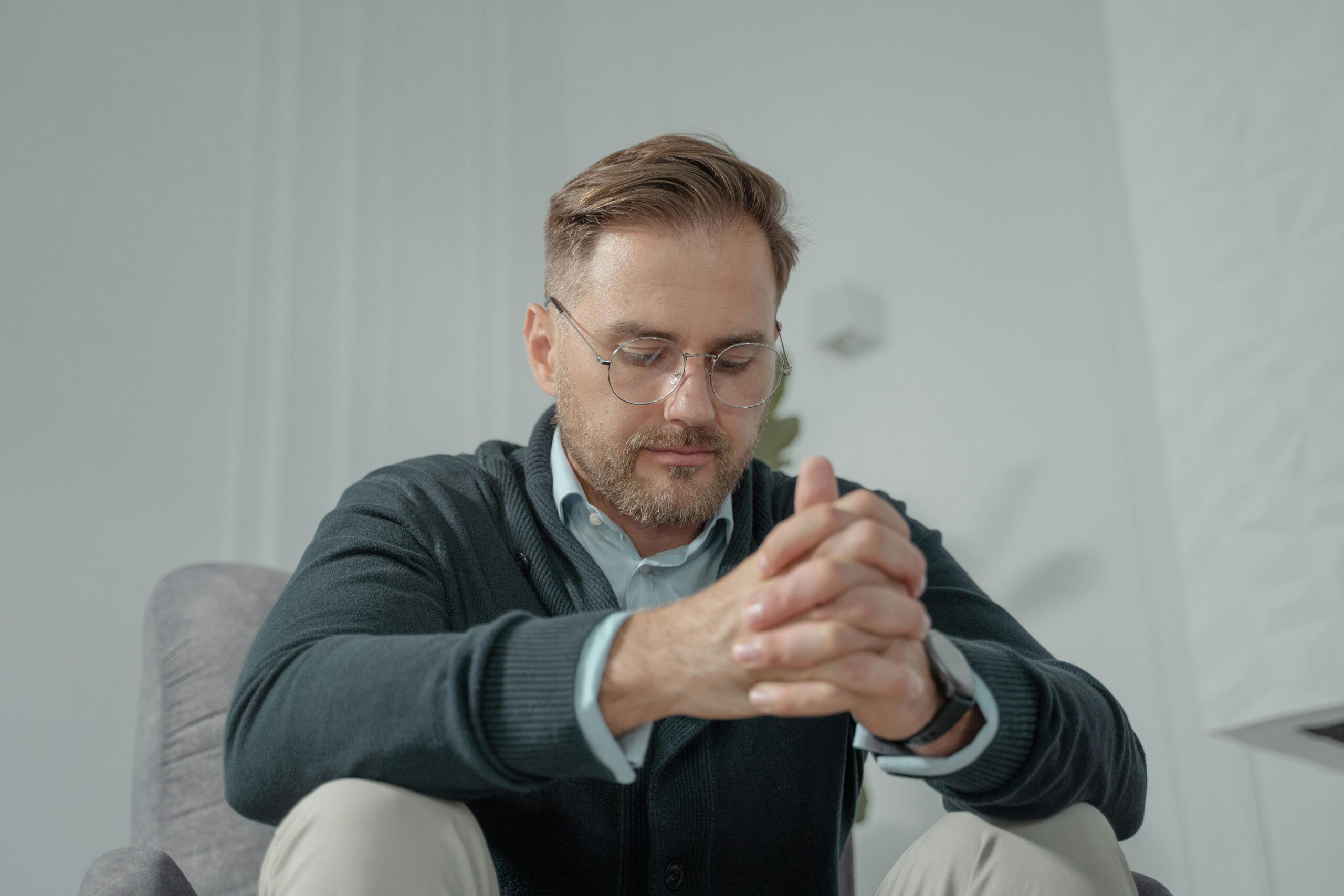 Man with glasses and hands clasped together, looking thoughtful, representing self-awareness developed in individual relationship counseling in Denver, CO.