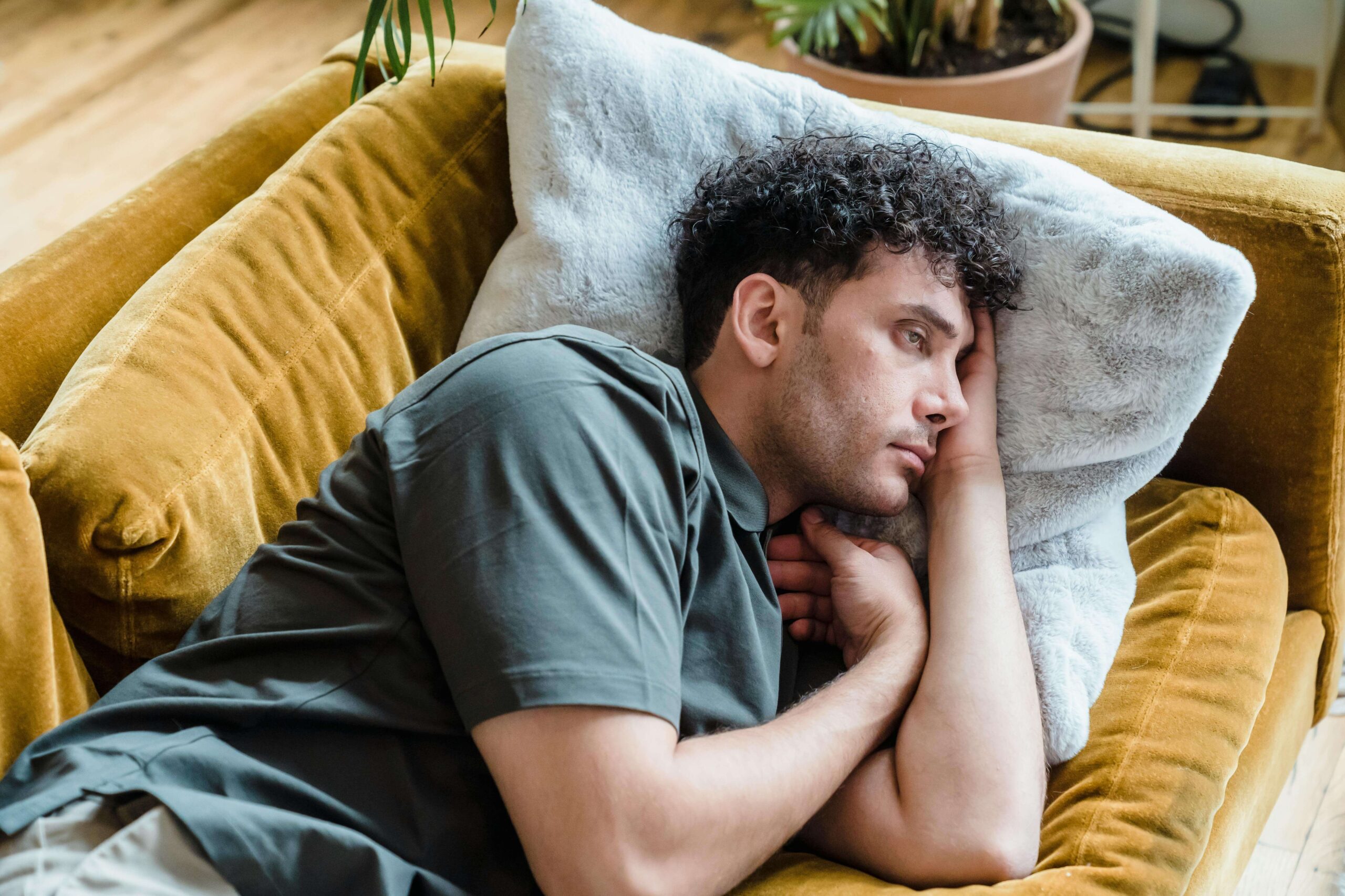 Man lying on a couch with his head on a pillow, appearing stressed and emotionally drained, illustrating patterns explored in therapy for relationship trauma in Denver, CO.